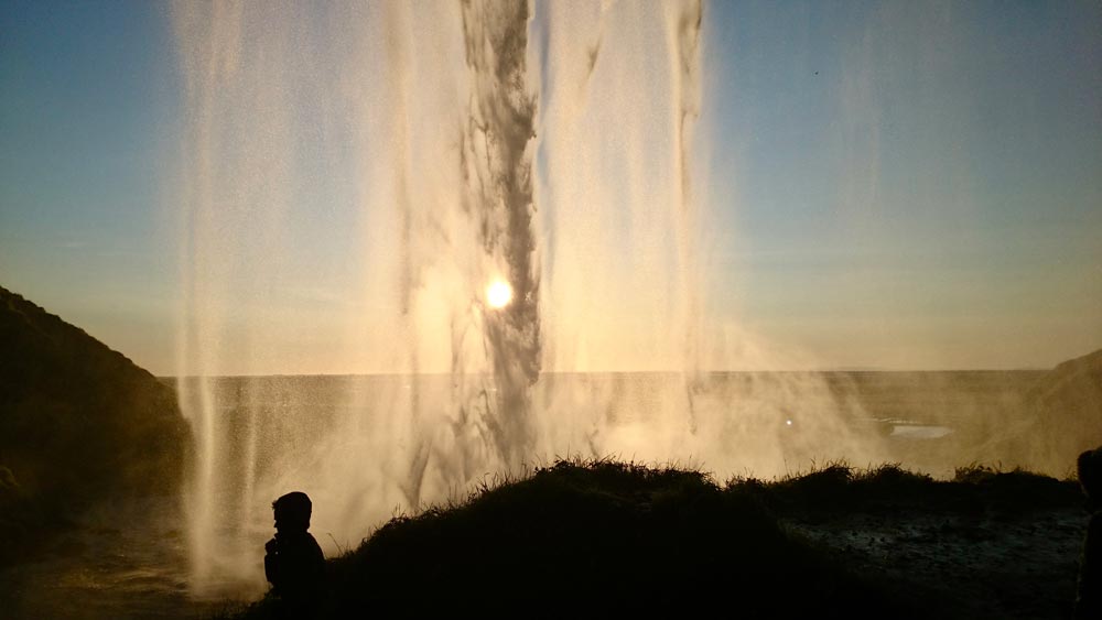 Seljalandsfoss waterfall standing behind sun shining through